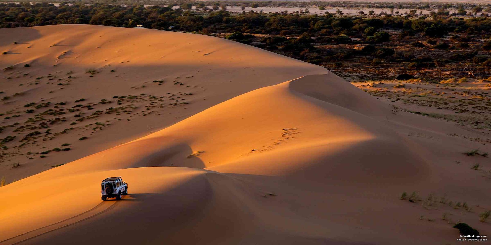 4x4 vehicle climbing red Namib desert dunes at golden hour, Namibia